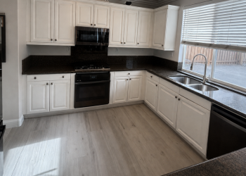Brighten up a dark kitchen with Cabinet Refacing Satin white refaced raised-panel cabinets with crown moulding and dark granite countertops