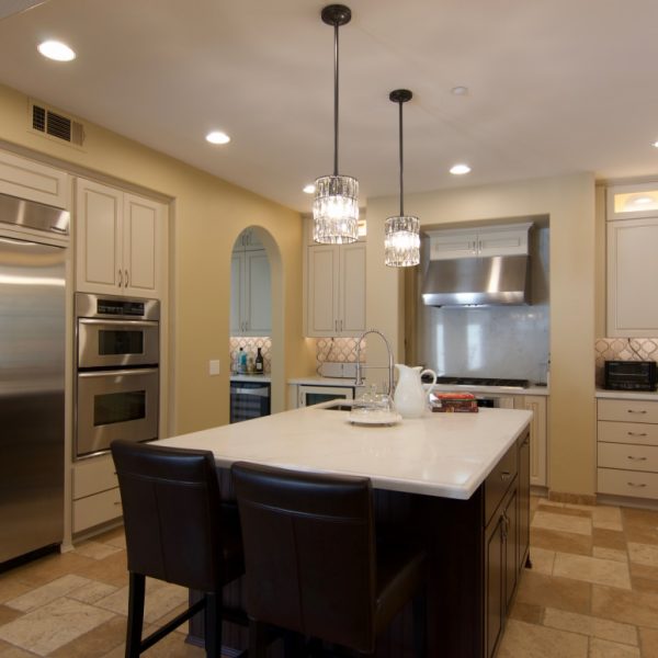 The same kitchen after refacing, with cream cabinets, a white quartz island and an arabesque tile backsplash